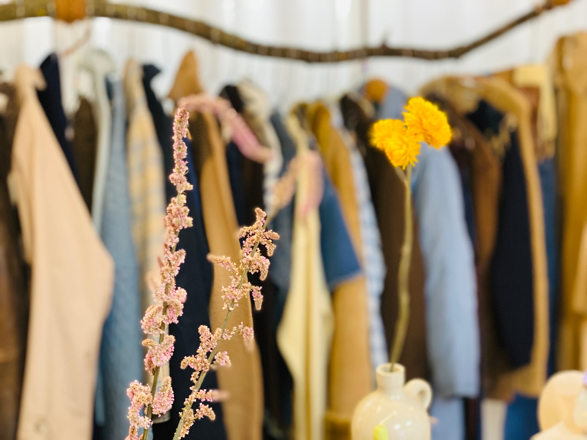 A warm rail of vintage clothing with dried flowers in an ethical boutique.